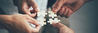 A photo of four hands, each holding a puzzle piece that fits with the others, meant to symbolize building Organizational Strategy Services offered by Ayuka Consulting.