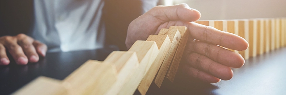 A hand stopping a line of small blocks of wood from continuing to fall into each other to represent Enabling Organizational Change services offered by Ayuka Consulting.